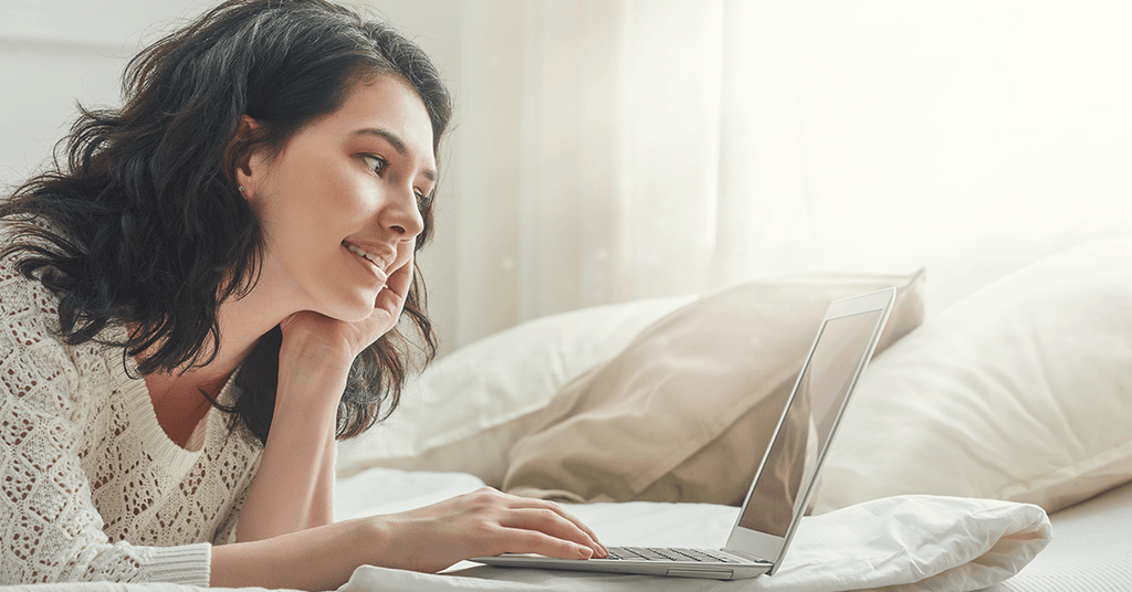 Woman lying on bed with her laptop doing research