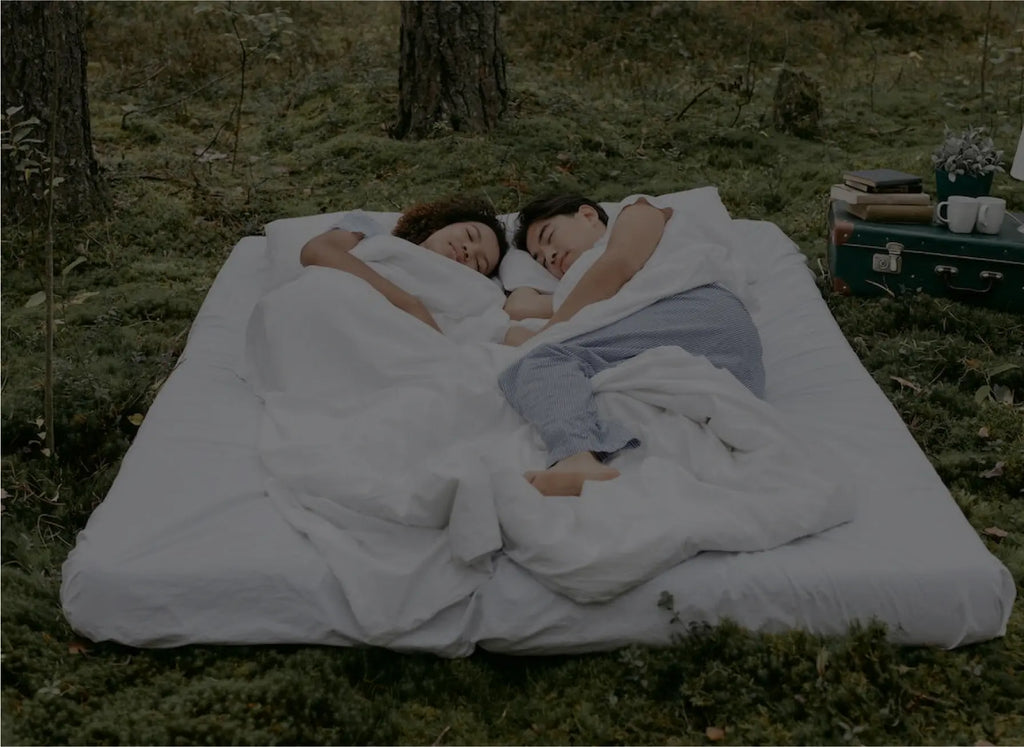 A couple sleeping outside in the cool fresh air. They are on a mattress on the ground