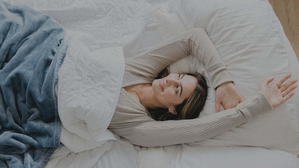 Woman waking up smiling and looking outside. Wearing a long sleeved PJ and a blue comforter