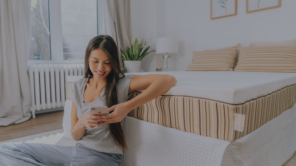 Woman sitting on the floor in front of her Essentia organic mattress with EMF Protection Foam using her cell phone