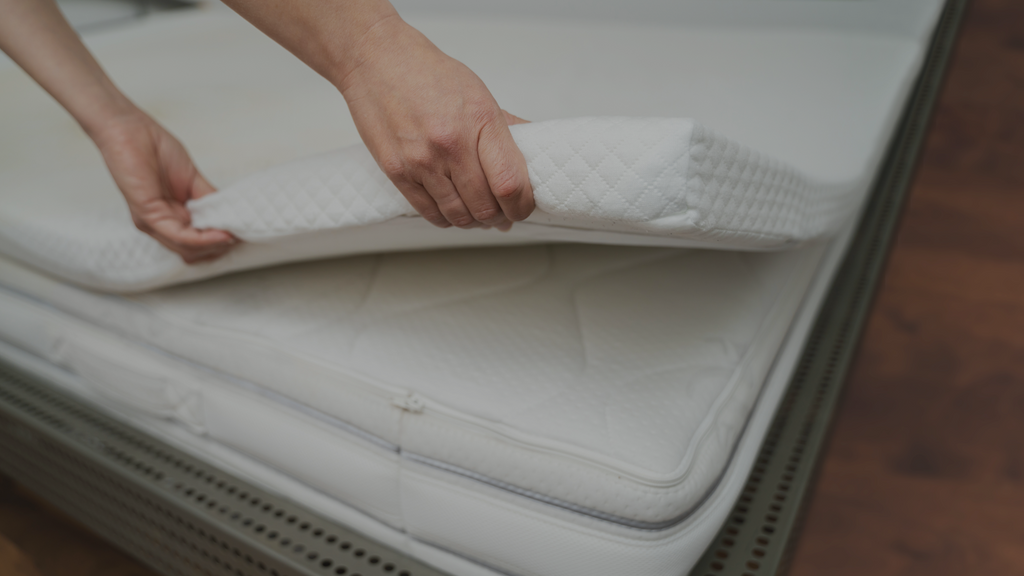 a mattress topper being lifted off the corner of a mattress.