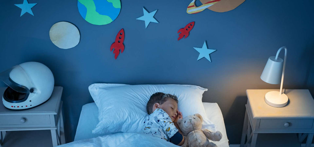 Young boy sleeping in his big kid bed in his space themed bedroom