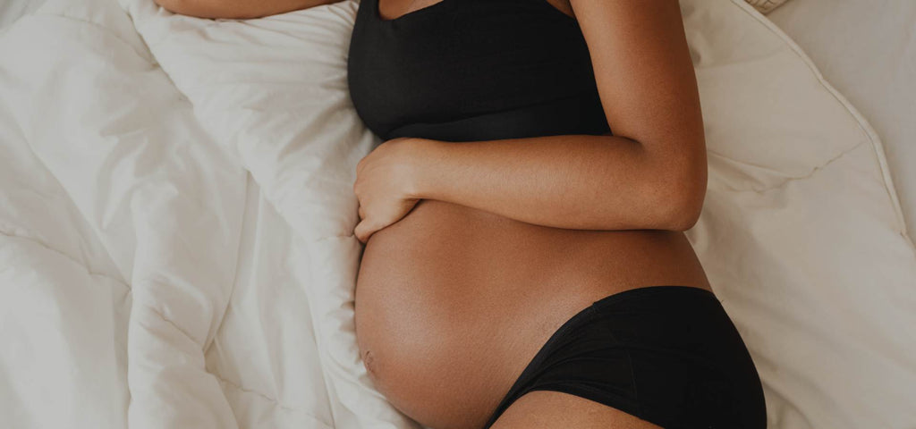 Woman sleeping on her side while cradling her exposed baby bump