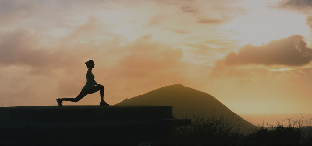 Woman stretching at sunset after hike in nature, supporting deep recovery and better sleep.