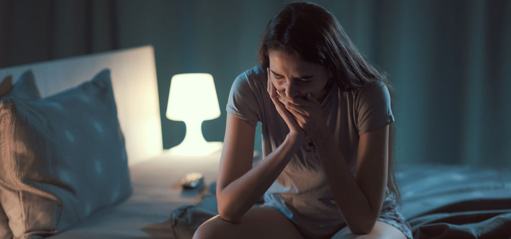 Woman sitting at the edge of her bed yawning.