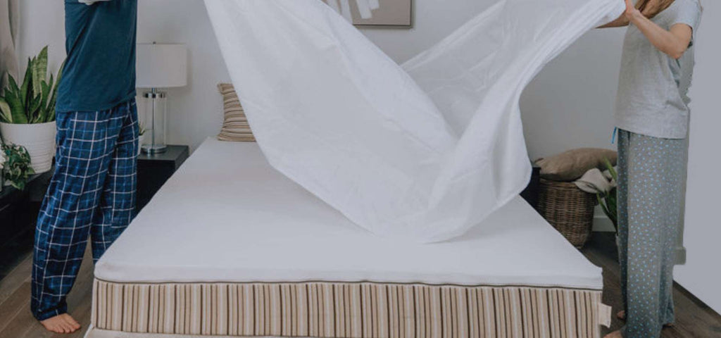 Couple putting white organic cotton sheets on their Essentia organic mattress