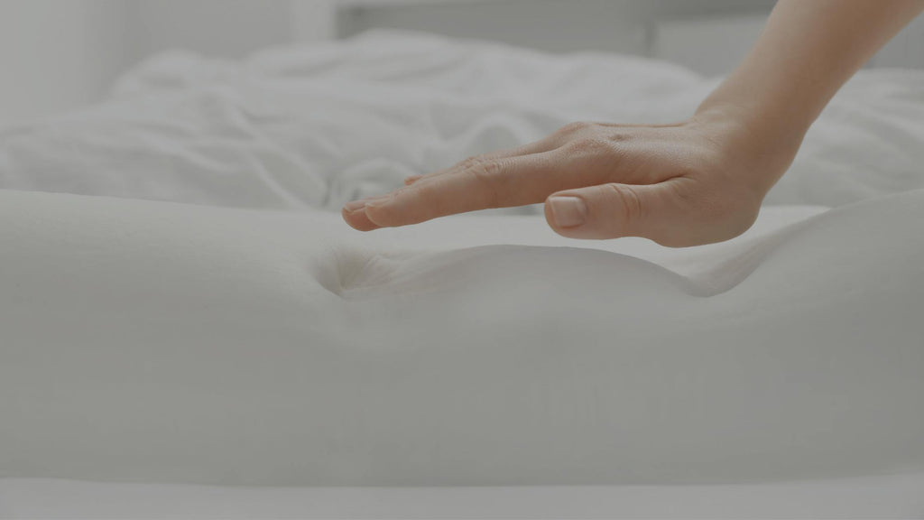 Woman's hand lifting after pushing down on a foam mattress. Her hand imprint is visible in the foam.