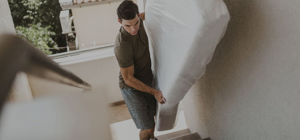 Man walking up stairs holding a twin size mattress
