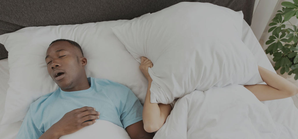Man snoring while wife covers her face with a pillow