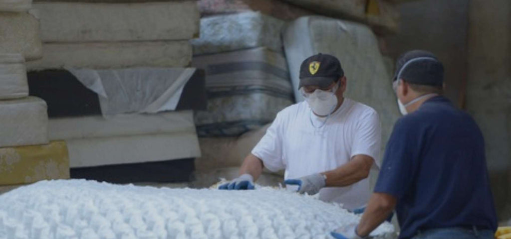 two men shown recycling a mattress with a stack of old mattresses behind them