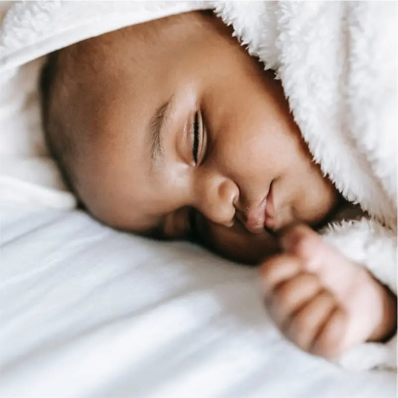 A baby fast asleep in a terry gown on an Essentia organic crib mattress.