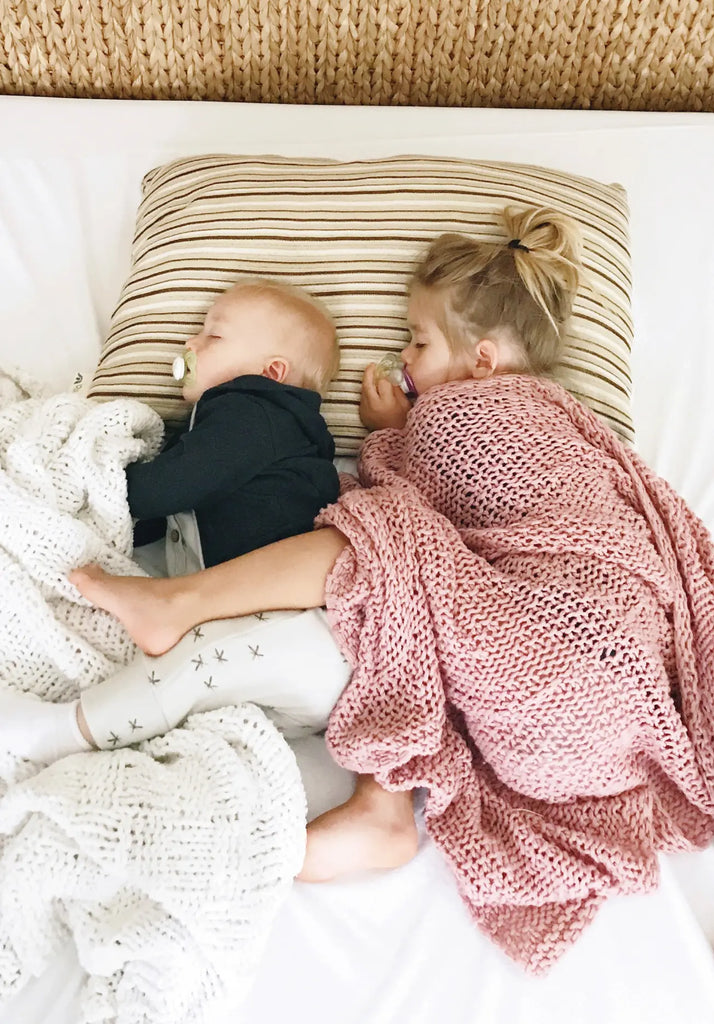 A child and a baby asleep on a bed with their heads on an Essentia pillow.
