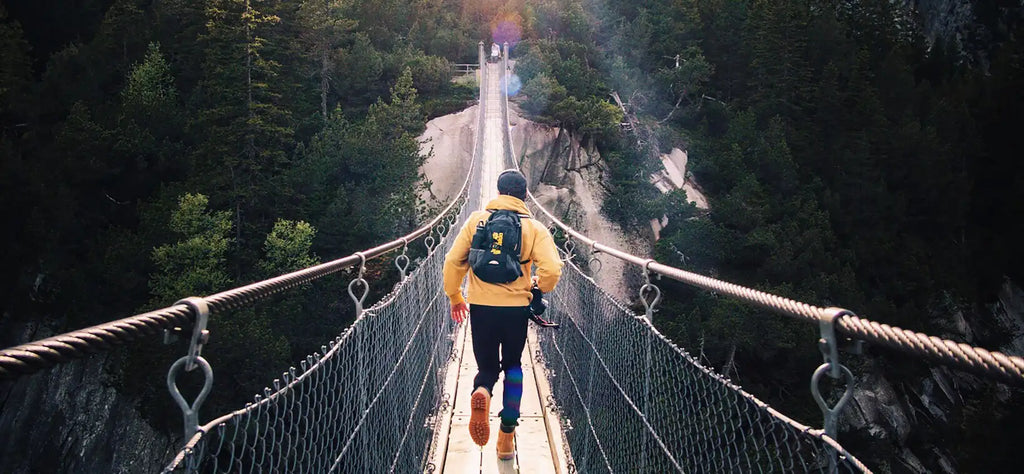 Hiker in a yellow jacket crossing a rope bridge
