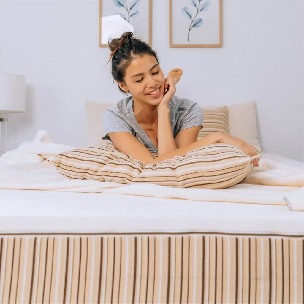 A young woman relaxing on a the REM5 Essentia organic mattress. She is resting her elbows on an Essentia pillow.