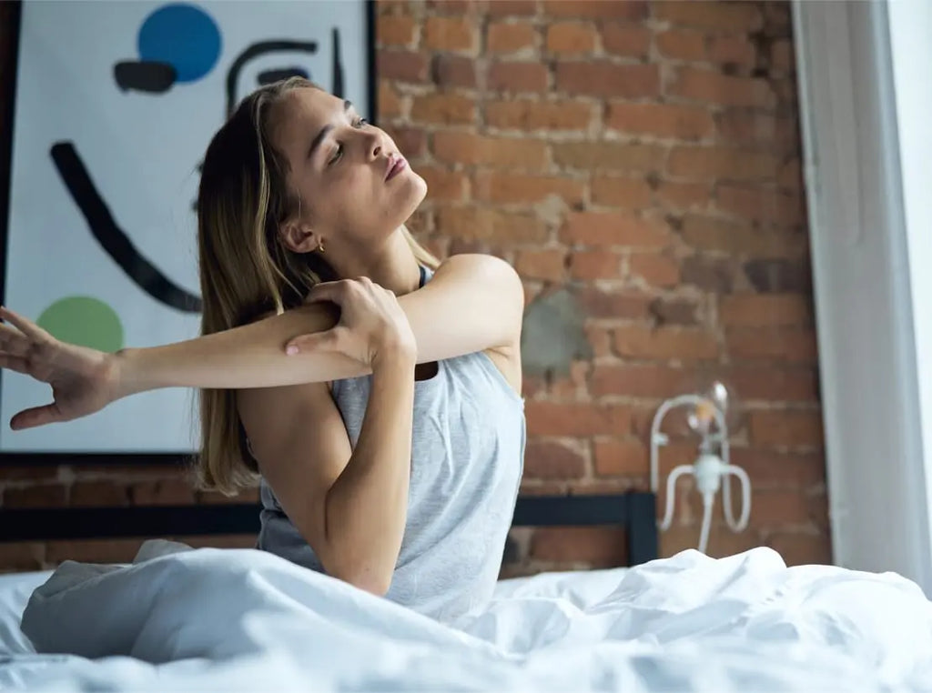 Woman in bed waking up refreshed and stretching her arm
