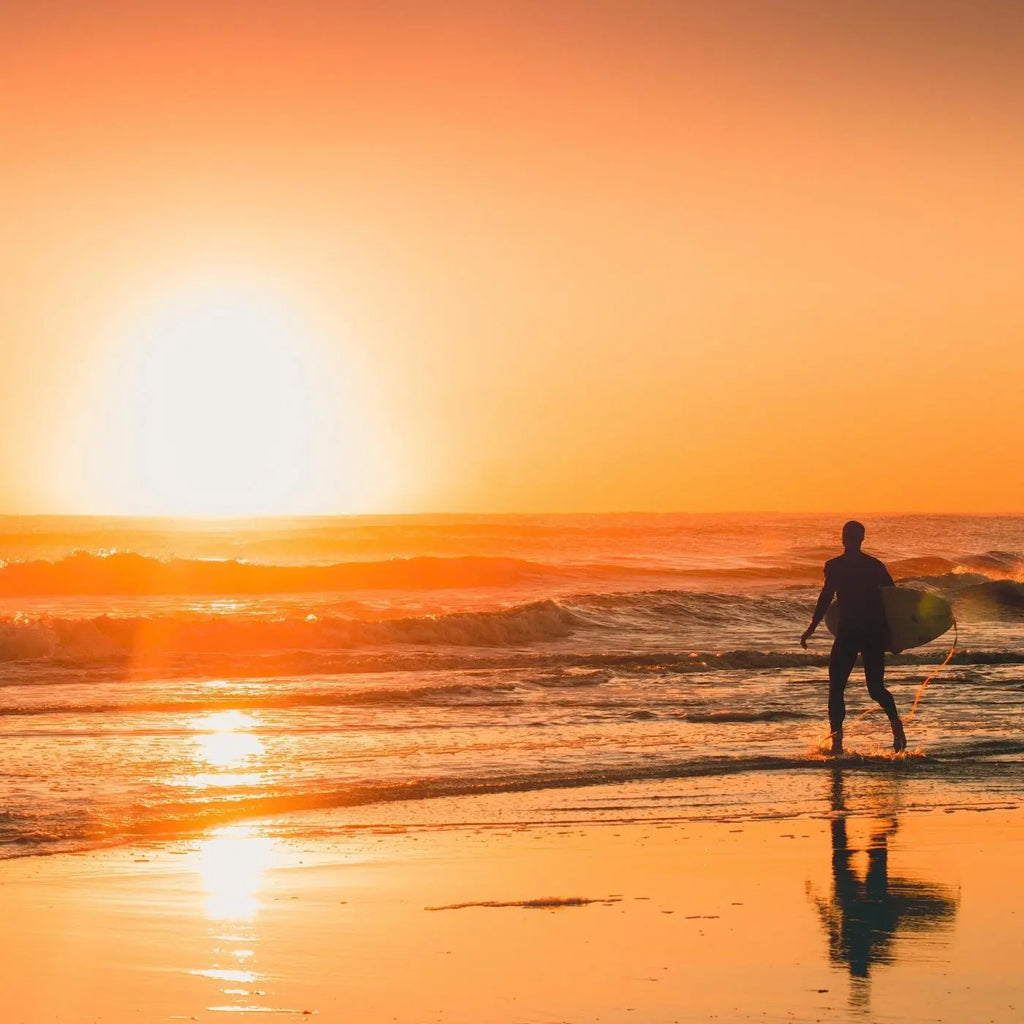 Surfer walking into the ocean at sunrise.